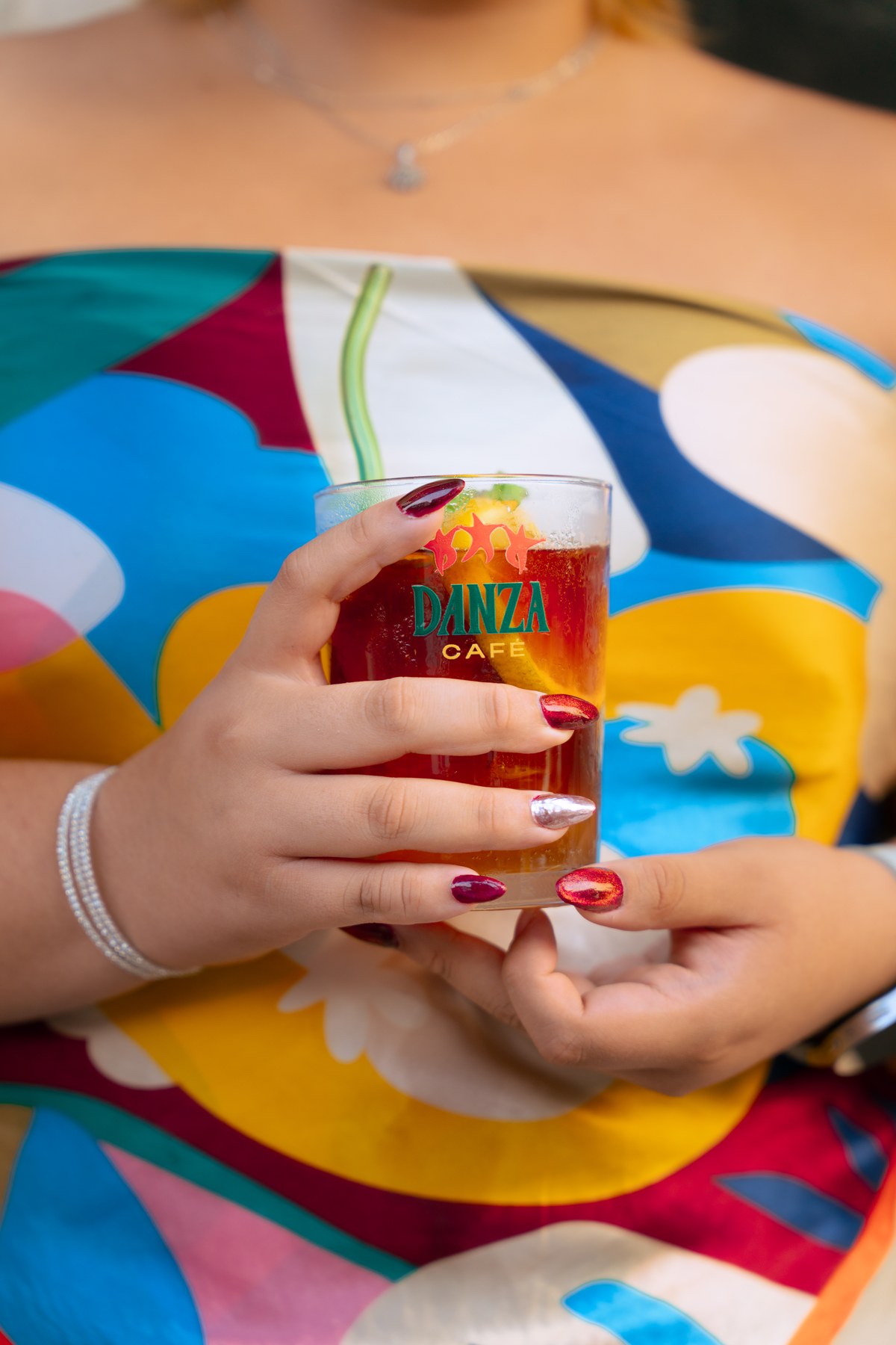 Patron wearing saturated geometric silk scarf holding branded Danza glassware with citrus espresso tonic